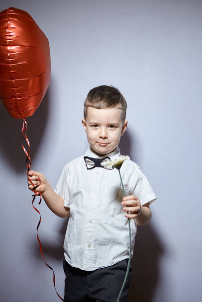 Valentine's day. Happy boy stands and holds red ball hearts on a white background.  - Fotoğraf, Görsel