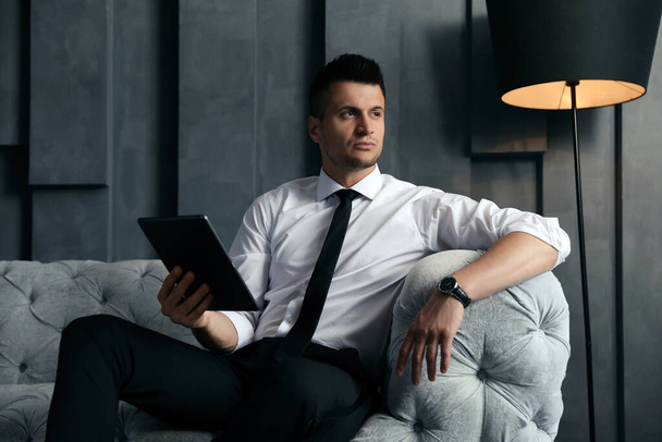 Handsome businessman with tablet on sofa indoors. Luxury lifestyle - Фото, изображение