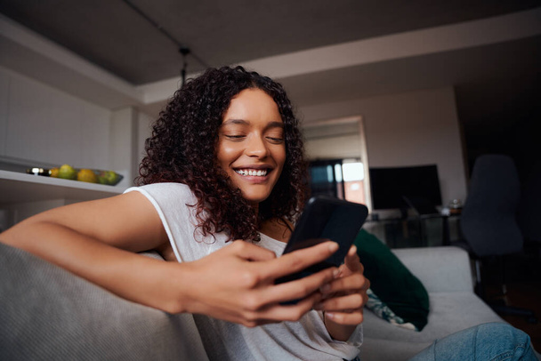 Mixed race female texting on cellular device smiling while relaxing at home - Fotografie, Obrázek