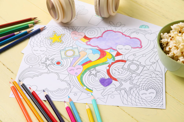 Цветной рисунок, попкорн, наушники и карандаши на деревянном фоне - Фото, изображение