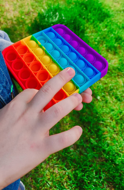 Trendy relaxing toy pop-it in boys hands. A kid is holding anti stress rainbow fidget toy popit. Popular game for adults and children. - Φωτογραφία, εικόνα