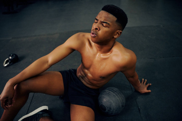 African American male resting on the gym floor after an intense cross fit session. Male athlete looking exhausted after the workout. High quality photo - Foto, Imagen