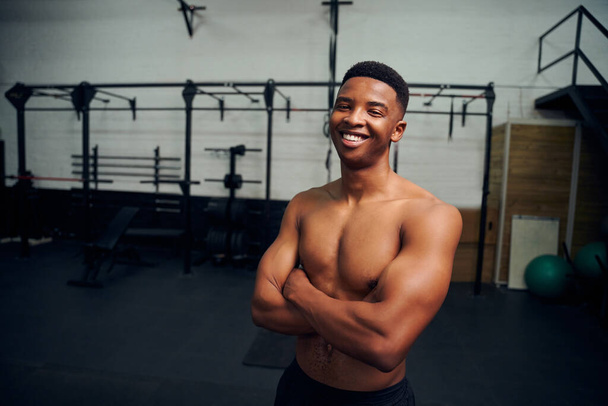 African American male standing with crossed arms and smiling to the camera. Male athlete looking happy while exercising in the gym. High quality photo  - 写真・画像