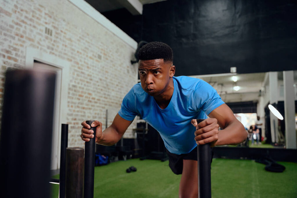 African American male working out intensely during cross fit training. Male athlete pushing the sled in the gym. High quality photo - Foto, imagen