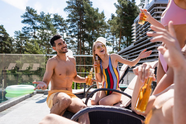 Cheerful interracial friends with beer talking near swimming pool  - Photo, Image