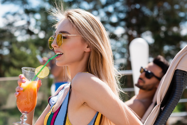 vrouw in zonnebril en badpak drinken cocktail buiten  - Foto, afbeelding