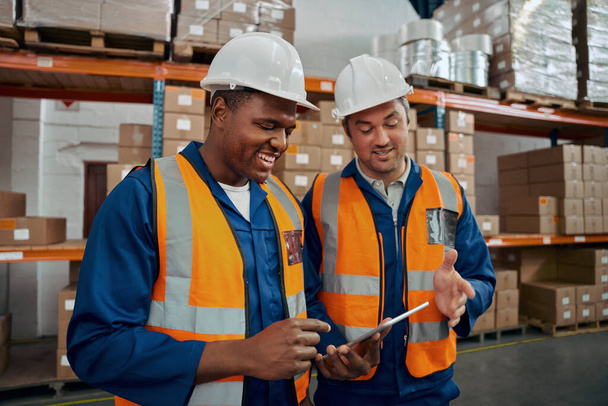 Happy industrial workers in white hardhat and protective vest looking at digital tablet - Photo, Image