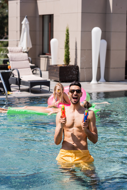 excited muslim man playing with water pistols near friends in pool - Fotó, kép