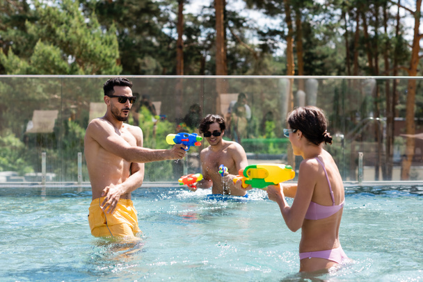 wielonarodowych przyjaciół bawiących się podczas bitwy pistoletów wodnych w basenie - Zdjęcie, obraz