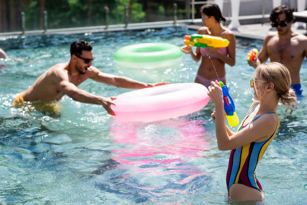 amici multiculturali divertirsi in piscina con anelli di nuoto e pistole ad acqua - Foto, immagini