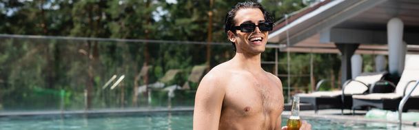 szczęśliwy człowiek bez koszuli w okularach przeciwsłonecznych relaksujący się w basenie z butelką piwa, baner - Zdjęcie, obraz