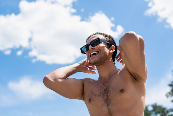 low angle view of happy shirtless man in sunglasses against blue cloudy sky - Fotoğraf, Görsel