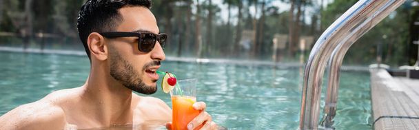 joven hombre musulmán en gafas de sol beber cóctel en la piscina, pancarta - Foto, Imagen