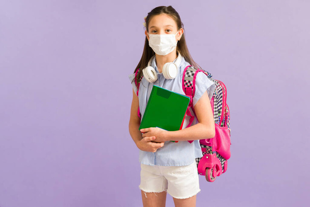 Умная девочка-подросток в маске для лица и наушниках, посещающая школу и предотвращающая распространение вируса - Фото, изображение