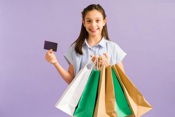Adorable preteen girl holding a credit card after paying at the mall. Cheerful little girl carrying a lot of shopping bags  - Foto, imagen