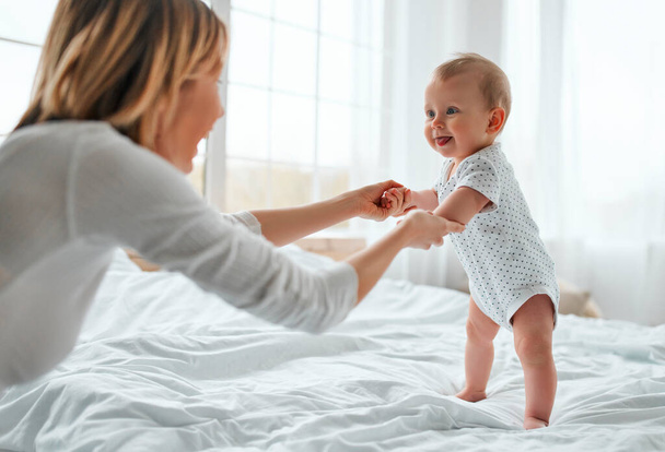 Loving mom carying of her newborn baby at home.Mother and child on a white bed. Mom and baby boy in diaper playing in sunny bedroom. Parent and little kid relaxing at home. Family having fun together. - Photo, Image