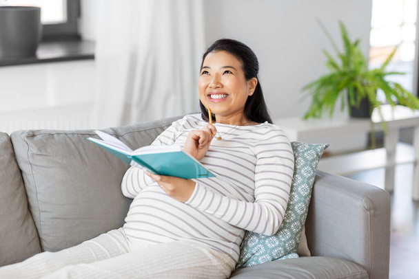 happy pregnant woman writing to diary at home - Foto, imagen