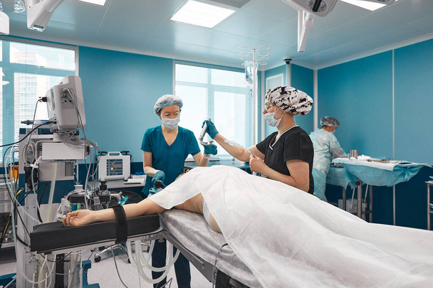 Equipos de un médico en un quirófano moderno, conecta al paciente a un dispositivo de ventilación pulmonar artificial, los anestesiólogos preparan al paciente para la cirugía pulmonar - Foto, imagen