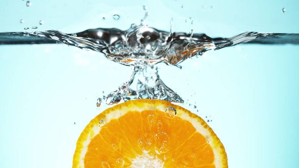 Fresh orange slice dropped into water with splash. Studio shot with clear background. - Фото, изображение
