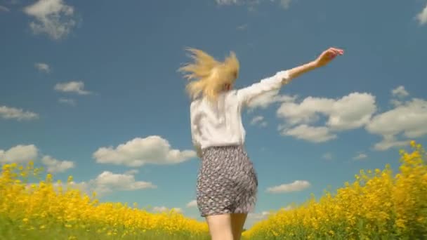 Een jonge vrouw rent door een veld van bloeiende koolzaad. - Video