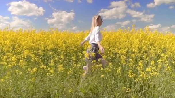 Kadın mutlu bir şekilde kolza tohumu tarlasında yürüyor ve sarı çiçeklere dokunuyor.. - Video, Çekim