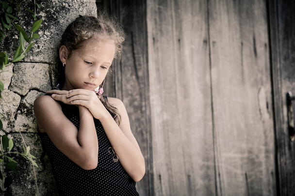 Portrait of sad little girl standing near stone wall in the day  - Фото, зображення