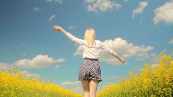 vrouw rent snel door weide van bloeiende koolzaad, glimlachend, haar armen open - Video