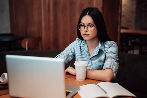 Woman sitting in cafe coffee break open space work computer laptop have lunch with documents papers. Lady dressed striped shirt stylish glasses speaking with colleagues in video voice chat copyspace - Photo, Image