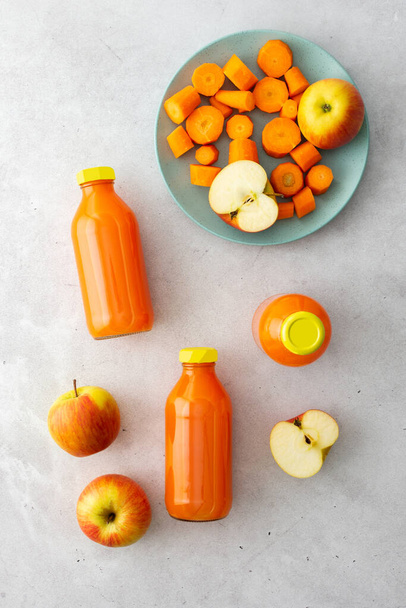 Zumo de manzana de zanahoria en botellas con manzanas frescas y zanahorias sobre un fondo gris, vista superior - Foto, Imagen