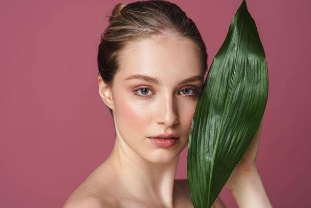 Beauty portrait of an attractive young woman posing with green leaf isolated over pink background - Fotografie, Obrázek