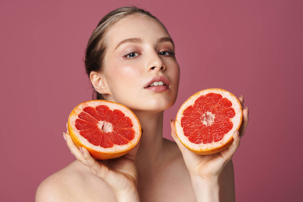 Beauty portrait of an attractive sensual young woman posing with grapefruit isolated over pink background - Photo, Image