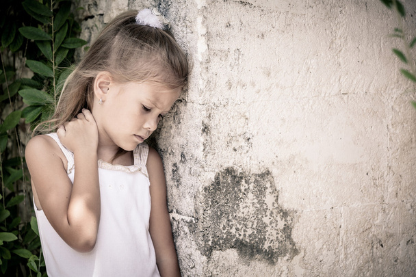 Portrait of sad little girl standing near stone wall in the day  - Foto, afbeelding