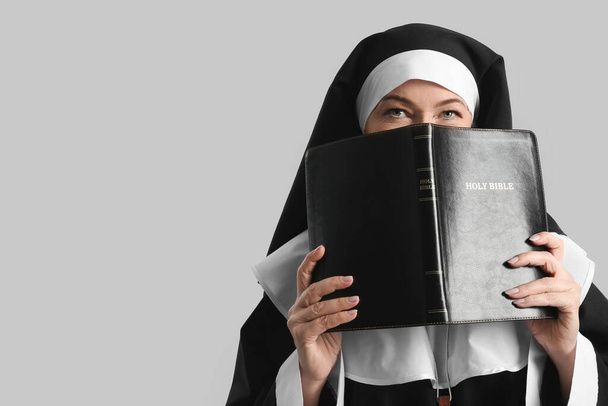 Monja madura con la Santa Biblia sobre fondo gris - Foto, imagen