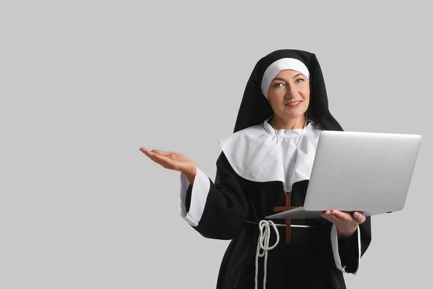 Mature nun with laptop on grey background - Фото, изображение