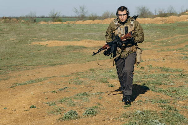 озброєний молодий білий чоловік у військовій формі носить навушники та окуляри на полігоні
 - Фото, зображення