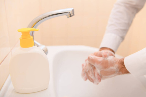 πλύσιμο στο χέρι με σαπούνι ή τζελ κάτω από τρεχούμενο νερό στο νιπτήρα, καθαριότητα και υγιεινή, αντρικά χέρια ντυμένα με λευκό πουκάμισο - Φωτογραφία, εικόνα