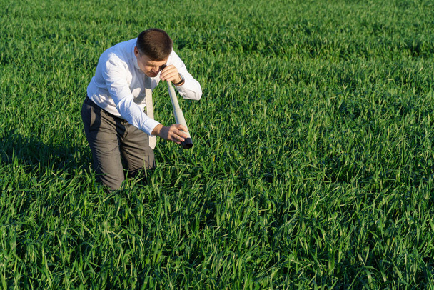 hombre de negocios posa con un catalejo, mira en la hierba y busca algo, hierba verde y cielo azul como fondo - Foto, imagen