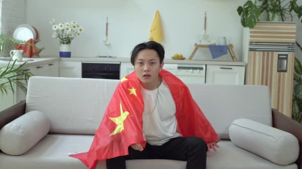 Un fanático del fútbol chino ve televisión en casa. Abanico deportivo emocional con la bandera de China - Imágenes, Vídeo