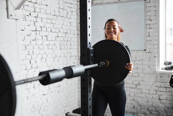 Jolly young woman working out with barbell - Foto, afbeelding