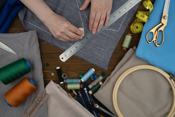Manos femeninas confeccionando ropa. Cortar y coser prendas personalizadas. Tijeras, accesorios de costura hilos, telas sobre una mesa de madera. - Foto, Imagen
