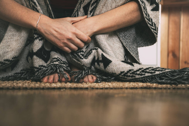 stopy i ręce kobiety siedzącej na dywanie na podłodze w ręcznie robionym ponczo. tło z przestrzenią kopiowania. medytacja koncepcyjna. obraz poziomy - Zdjęcie, obraz
