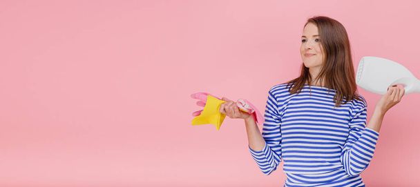 Shot lány tartsa mosószer és gumikesztyű szivacs boldog álomszerű kifejezés felett rózsaszín háttér testbeszéd - Fotó, kép