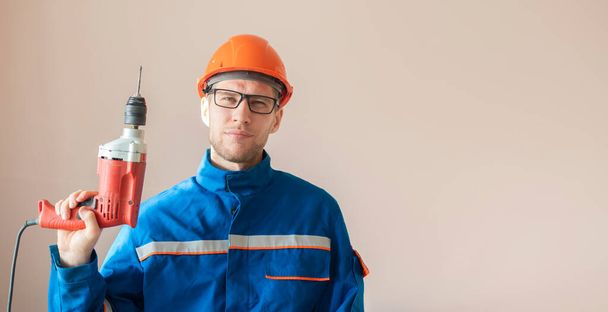 νεαρός άνδρας εργάτης με στολή που κρατά την άσκηση ηλεκτρικού εργαλείου - Φωτογραφία, εικόνα