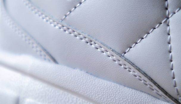 Primer plano de tela sintética con costuras de diamante blanco y suela de goma blanca. Zapatos deportivos. Tejido acolchado en color blanco o claro, textura - Foto, imagen