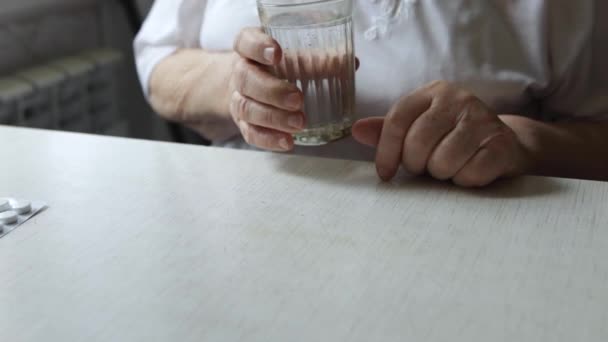Traurige alte Frau, die Tabletten nimmt, gesundheitliche Probleme im Alter, teure Medikamente. Die Hände einer älteren Frau beim Auspacken mehrerer Tabletten zur Einnahme von Medikamenten. Oma nimmt Tablette und trinkt ein Glas Wasser - Filmmaterial, Video
