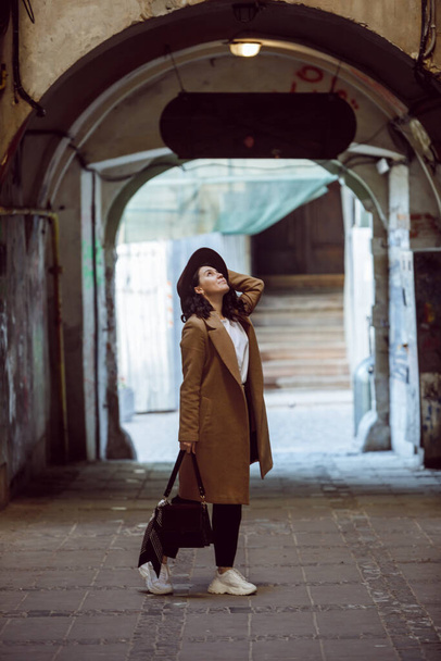 woman in stylish coat and hat walking by small european street copy space - Φωτογραφία, εικόνα