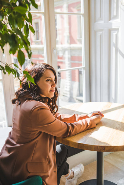 vrouw zitten in cafe in de buurt van venster kopiëren ruimte wachten - Foto, afbeelding