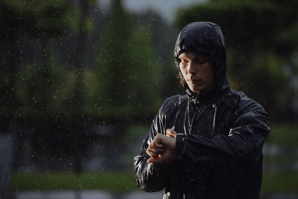Jogger looks a time on his watch under rain, flash light - Foto, afbeelding