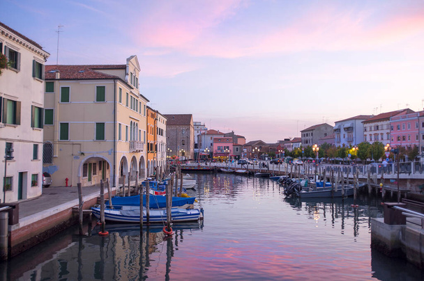 CHIOGGIA, ITALIEN - 15. SEPTEMBER 2019: Der Hauptkanal der Stadt Chioggia, genannt Klein Venedig, mit seinen Booten, die die angrenzenden Gebäude und Geschäfte an der Oberfläche widerspiegeln, bei Sonnenuntergang - Foto, Bild