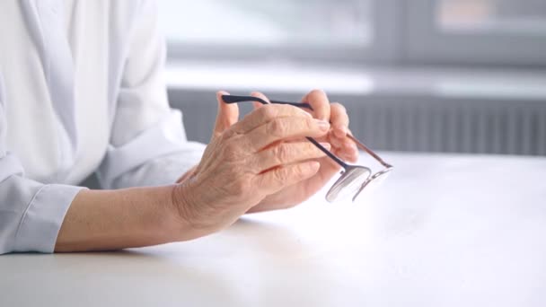 Reszkető öreg hölgy ráncos kezét tartsa szemüveg felett asztal - Felvétel, videó